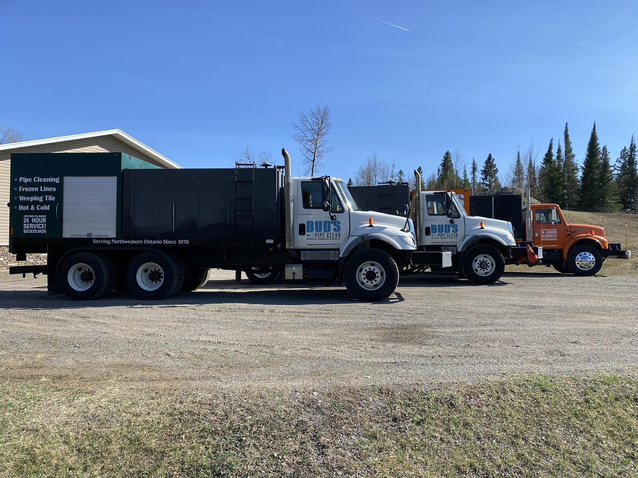 3 cleaning trucks in front of a garage in the summer with Bud's Pipe Clean logo on the side and blue sky in the background